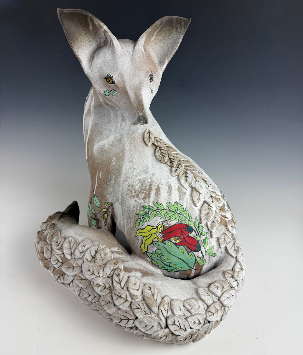 A sculpted ceramic white fox with a textured, leaf-patterned tail and accents of flowers and leaves on the body and the face.